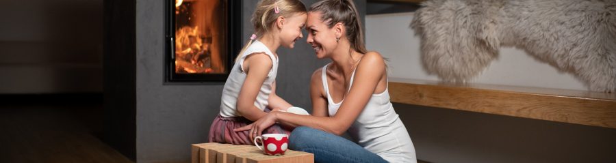 Žena maminka sedící s dítětem u teplého krbu v popředí cihla Porotherm T Profi