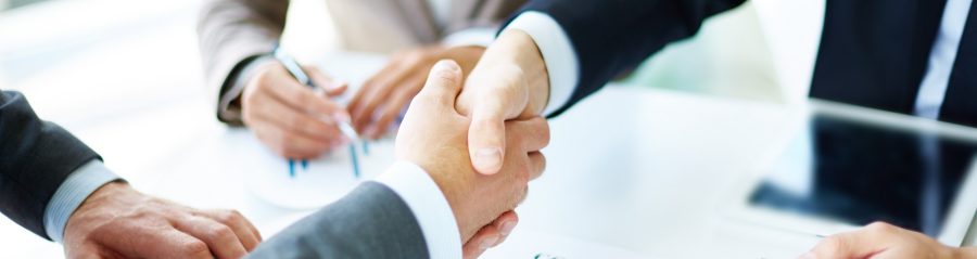 Image of business partners handshaking over business objects on workplace