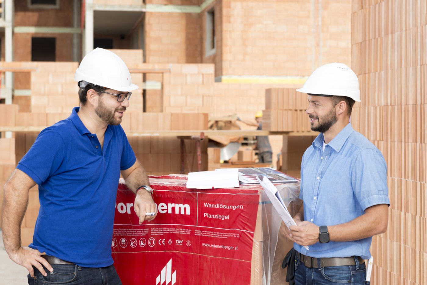 Building professionals talking at construction site next to foil wrapped pallette of brick blocks. > There is another version of this image available with another worker in the background