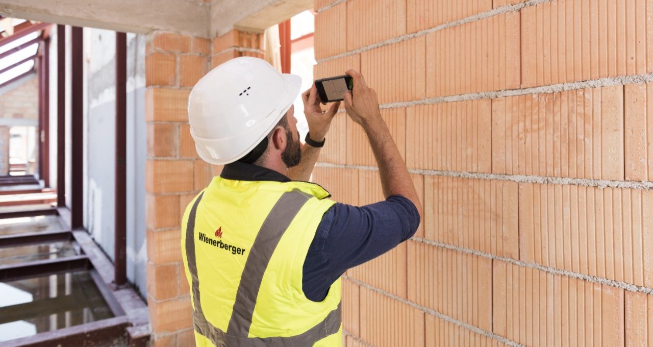 Builder whith saftey jacket and hard hat taking picture of bare brick wall