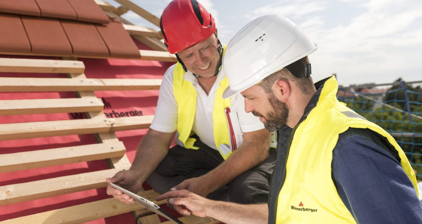 Urban roofer and product manager with tablet computer explaining product advantages to urban roofers wearing safety jackets and hard hats